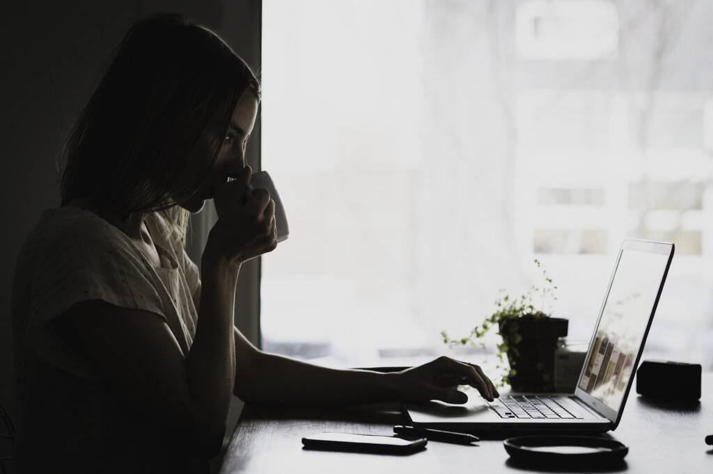 Jeune femme concentrée lisant des informations juridiques sur son ordinateur tout en buvant un café, symbole de vigilance dans un divorce amiable.